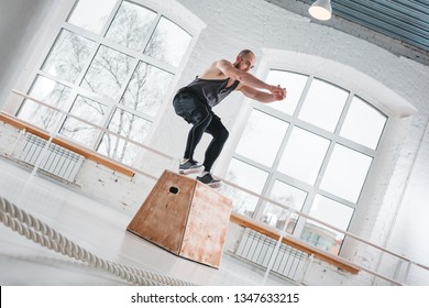 Strong man doing jumping exercises over box at a cross training style gym. Fit sportsman jump at box in workout gym