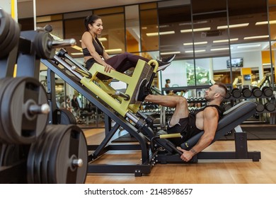 Strong man doing leg press in exercise machine to woman sitting on it in gym