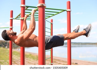 Strong man doing statics exercise on horizontal bar, having workout outdoors at sunny day
