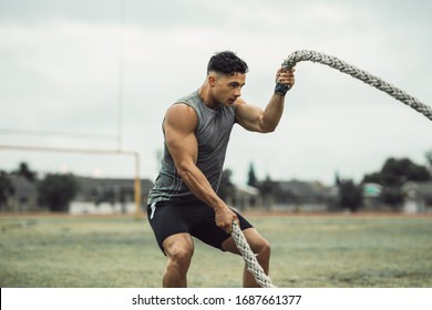 Strong man exercising with battle ropes. Athlete doing battle rope workout outdoors on a field.