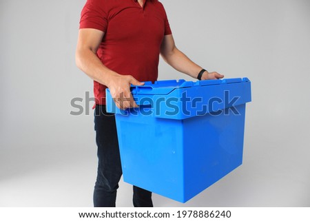 A strong man is holding a box. Plastic container for delivery. Ecological transportation of goods. Reusable box. Man's strong hands hold the box.
