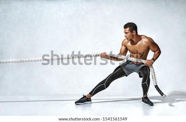 Strong man pulling\
rope. Photo of sporty man on grey background. Strength and\
motivation. Side view. Full\
length