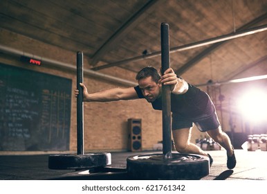 Strong man pushing heavy bogie with weight disks. Horizontal indoors shot