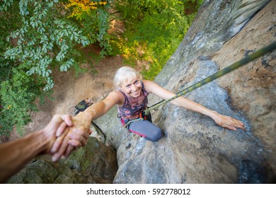 Strong man rock climber is helping to older smiling woman climber to reach a top of the rock. Man giving a hand to the woman. View from the top - Powered by Shutterstock