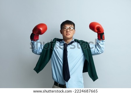 Strong Man Showing Bieceps. Portrait of Asian Guy Demonstrating Power in His Hands, Showing Biceps, Feeling Energy to Win Success. Indoor Studio Shot Isolated on Grey Background 