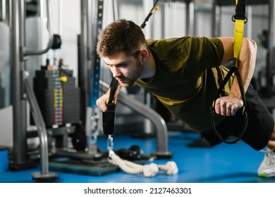 Strong man in sportswear doing push ups with trx fitness straps. Young fit man at hands training in gym, healthy lifestyle, modern crossover equipment and interior for sports workout exercises.