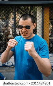 Strong man in sunglasses with fists raised on street - Shutterstock ID 2311424201