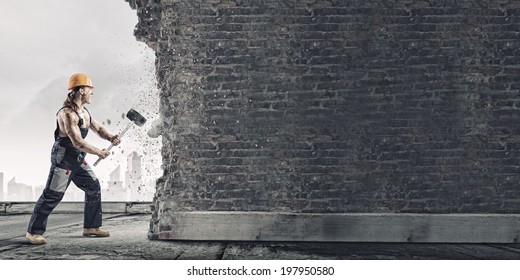 Strong Man In Uniform Breaking Brick Wall With Hammer