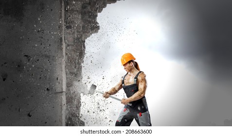 Strong Man In Uniform Breaking Brick Wall With Hammer