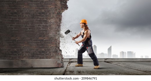 Strong Man In Uniform Breaking Brick Wall With Hammer