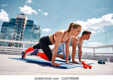 Strong man and woman are doing climber exercise while staying in plank position. They are training together on sunny roof among city center. Enjoying fitness with partner on sunny day concept - Powered by Shutterstock