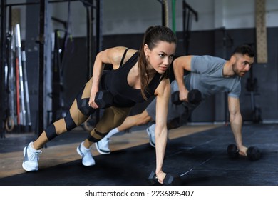 Strong man and woman holding dumbbells in plank position at the gym
