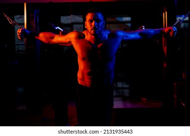 Strong Man Working Out With Dumbbell. Athlete In The Gym Training With Dumbbells. Abs And Biceps. Muscular Man On Blue Background With Dumbbell