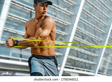 Strong man working with resistance band. Photo of man with athletic body training in the city. Strength and motivation