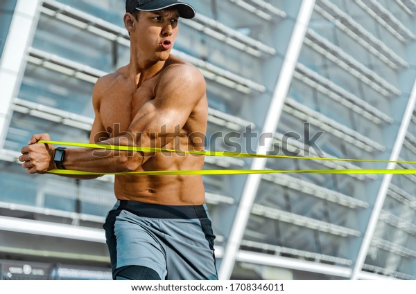 Strong man\
working with resistance band. Photo of man with athletic body\
training in the city. Strength and\
motivation