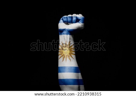 Strong man's hand in battle signal with Uruguay flag on black background.
