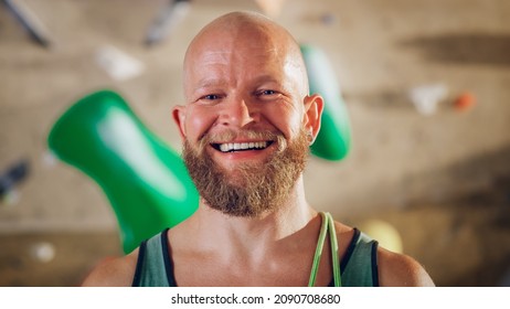 Strong Masculine Male Athlete Smiling And Posing At Rock Climbing Gym With Bouldering Wall Background. Handsome Happy Bald Man With Ginger Beard Portrait, Wearing Colorful Undershirt.