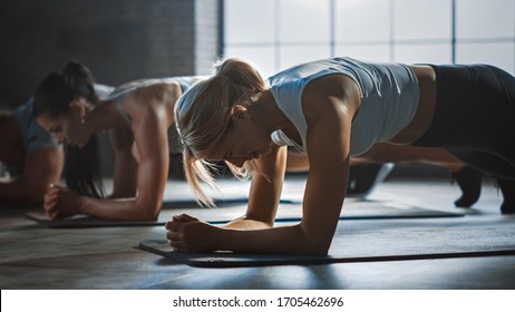 Strong Masculine Man And Two Fit Atletic Women Hold A Plank Position In Order To Exercise Their Core Strength. Young Blond Girl Is In The Foreground. They Workout In A Loft Gym.