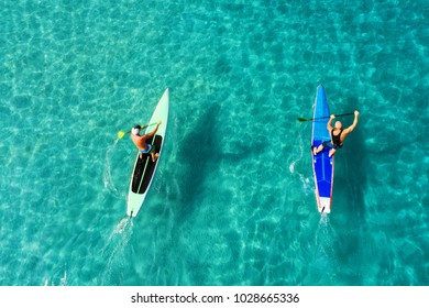 Strong men floating on a SUP boards in a beautiful bay on a sunny day. Aerial view of the men crosses the bay using the paddleboard. Water sports, competitions. Nai Harn beach, Phuket, Thailand.