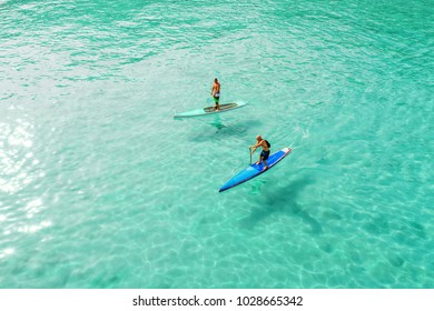 Strong men floating on a SUP boards in a beautiful bay on a sunny day. Aerial view of the men crosses the bay using the paddleboard. Water sports, competitions. Nai Harn beach, Phuket, Thailand. - Powered by Shutterstock