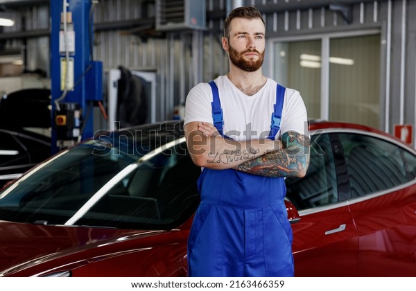 Strong minded young male professional technician car\
mechanic man in denim blue overalls white t-shirt hold hands\
crossed folded work in modern vehicle repair shop workshop indoor\
Tattoo translate fun