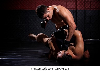 Strong MMA fighter holding his rival down and throwing punches at him during a fight. With plenty of copy space