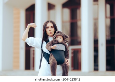 Strong Mom Walking Her Cute Infant In Baby Carrier. Funny Super Strong Mother Holding Her Baby Flexing Muscles With Confidence
