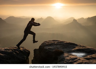 Strong mountain climber hiking and jumping over  the summit ridge of a peaks at sunset. Man takes leap of faith off of rock outcropping. Extreme sport
