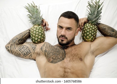 Strong muscular bearded man holding pineapples. Sexy tattooed hot man with tropical fruits. Portrait of topless handsome man with two pineapples