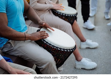 A strong muscular guy drums on a djemba, a street musician, drummers beat the rhythm of jazz in public, hands play on percussion. High quality photo