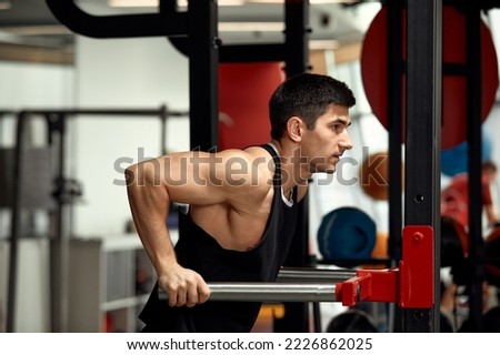 Strong muscular man doing push-ups on uneven bars in gym. Workout lifestyle concept.