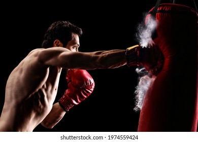 Strong muscular man punching a bag with boxing gloves on a black background