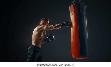 Un hombre fuerte de la musculatura pinchando una bolsa con guantes de boxeo. Aislado. Boxeador masculino golpeando una bolsa de boxeo en un gimnasio.