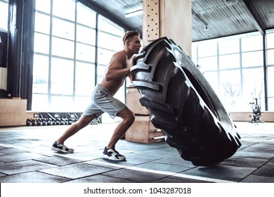 Strong Muscular Man Is Working Out In Gym. Cross Fit Training. Pushing Tire.