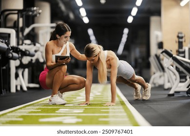 Strong muscular sportswoman in shape doing pushups in a gym while her coach is tracking progress on tablet. - Powered by Shutterstock