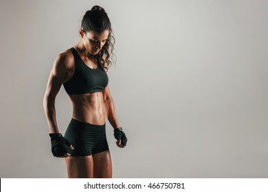 Strong Muscular Woman In Tight Black Shorts And Weight Lifting Gloves Over Gray Background With Copy Space