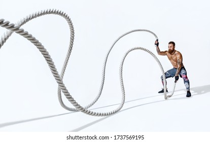 Strong muscular woman working out with battle ropes. Photo of handsome man with perfect body on white background. Strength and motivation. Full length
