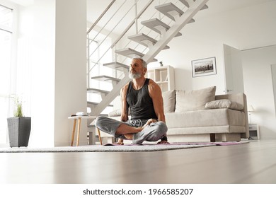 Strong older mid aged tattooed yogi man doing yoga exercises at home.Fit healthy mature senior tattooed male meditating relaxing lifting himself over mat sitting in yoga pose in living room at home.