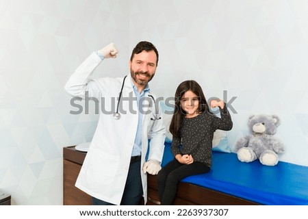 Strong pediatrician doctor and brave little girl doing a bicep curl looking happy after getting an allergy vaccine shot