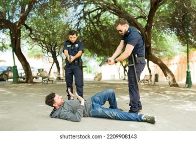 Strong Police Cops Arresting A Criminal Suspect Lying On The Floor After A Chase While Pointing Their Guns 