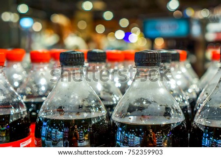 strong rows with clean plastic bottles with black sweet liquid. big army of bottles with red and black covers in grocery shop. plastic bottles with soft drinks background