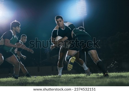 Strong rugby players fighting for the ball during the game. Intense rugby action under lights at sports arena.