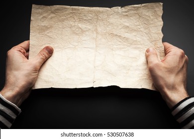 Strong Sailor Hands Hold Empty Old Crumpled Paper Sheet Over Black Background, Pirate Map Copy-space Template