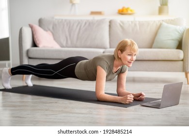 Strong Senior Woman Standing In Elbow Plank On Yoga Mat, Working Out To Online Sports Video At Home. Fit Mature Lady Exercising Her Core Muscles, Doing Domestic Fitness During Covid Quarantine