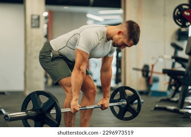 A strong sportsman is bending and lifting heavy weights in a sports center. A bodybuilder with big muscles is doing deadlifts in a gym. A weightlifter is performing strength exercises with a barbell. - Powered by Shutterstock