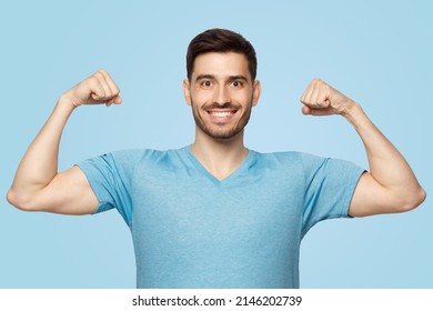 Strong and sporty athletic man in casua t-shirt, showing two biceps after training in gym, isolated on blue background