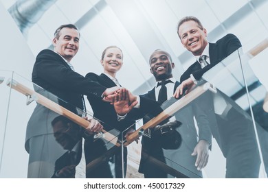 Strong And Successful Business Team. Low Angle View Of Four Confident Business People Standing Close To Each Other And Holding Hands Together