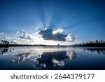 Strong sun rays behind cloud over Pine Glades Lake in Everglades National Park, Florida reflected in Calm water of lake.