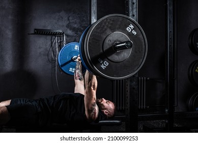 Strong sweaty muscular athlete fit active man doing hardcore bench press with heavy barbell weights in the gym. Active male bodybuilder workout and cross training concept. Real people exercise