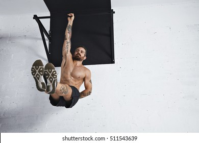 Strong Tattooed In White Unlabeled Tank T-shirt Male Athlete Shows Calisthenic Moves Hanging On Pull Bar One Arm Leg Raises Or L-sit Hold